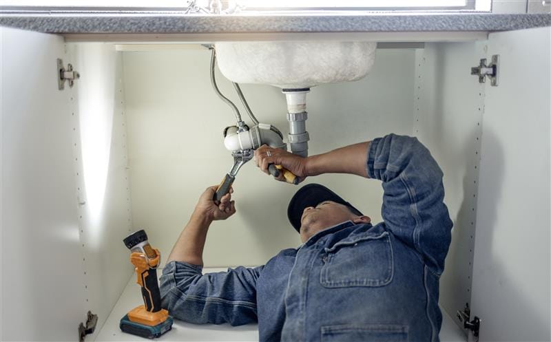 Plumber repairing pipes beneath a bathroom sink in Long Beach